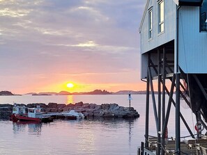 A pier with boats docked, a lighthouse, and a sunset over the water. - 8 Person Holiday Home in Hellesoy (Oygarden)
