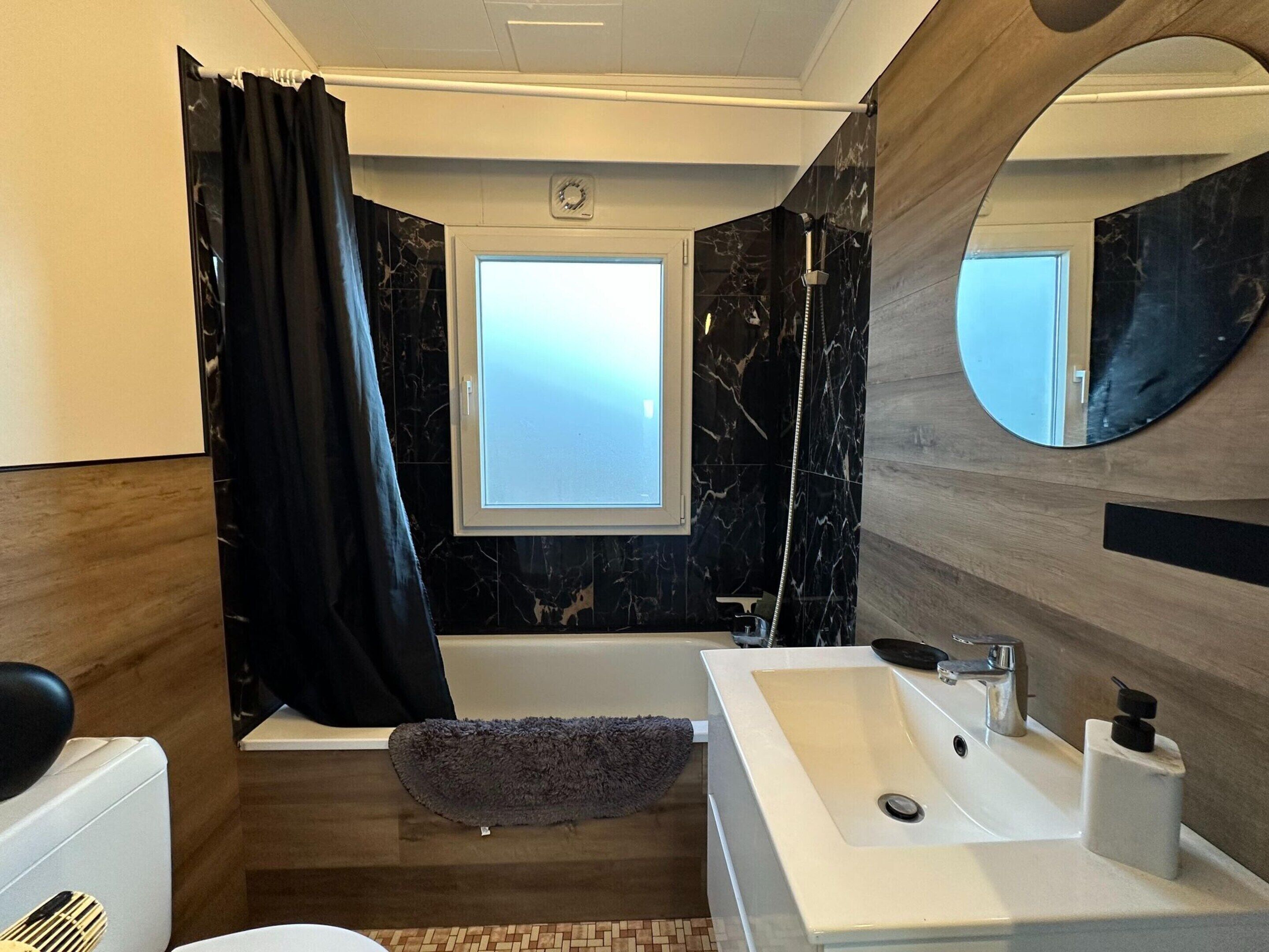 A modern bathroom with a bathtub, a large mirror, and a window.