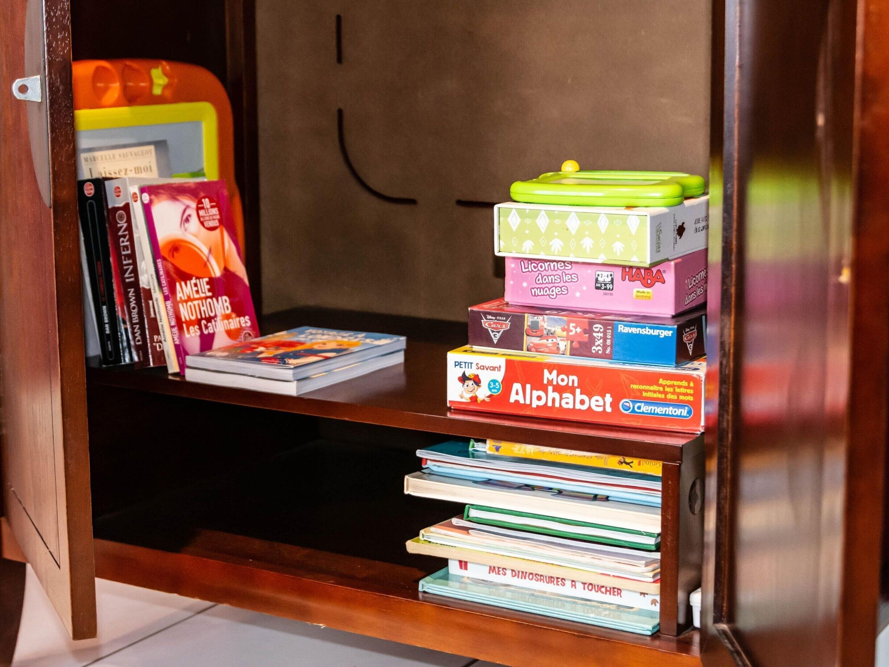 Une étagère en bois contenant divers livres et jouets éducatifs, notamment une boîte intitulée « Mon alphabet » et un livre intitulé « Mes dinosaures à toucher ».