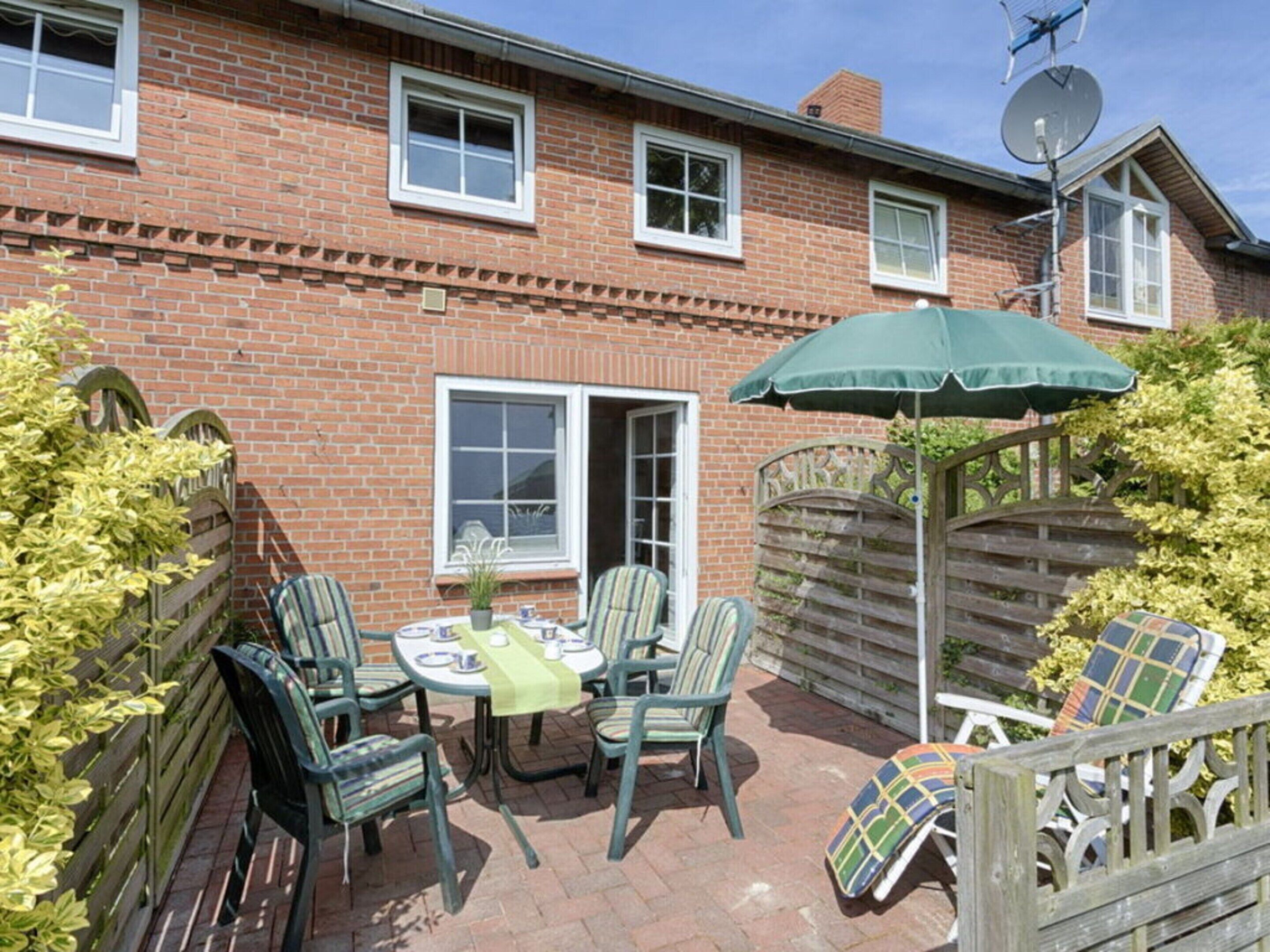 A brick house with a patio area featuring a round table and chairs, a green umbrella, and a wooden fence.
