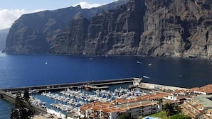 A marina with boats docked, a coastal town with buildings, and a mountain in the background. - Apartment Tenerife Near Sea & Pool (Santiago del Teide)