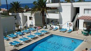 A swimming pool with sun loungers and umbrellas, surrounded by a white building with a view of the ocean. - Apartment Tenerife Near Sea & Pool (Santiago del Teide)