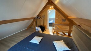 Un dormitorio acogedor en el ático, con techo inclinado, vigas de madera y una cama con almohadas.