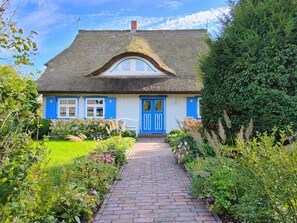 Een traditioneel huis met rieten dak, een blauwe deur en een pad van bakstenen dat naar de ingang leidt.