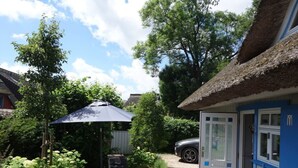 A backyard with a patio, a thatched-roof structure, and a car parked outside. - Captain House South Cats 8 (Wieck auf dem Darss)