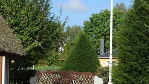 A pathway leading to a building with a thatched roof, surrounded by greenery and a flagpole with a flag. - Captain House South Cats 8 (Wieck auf dem Darss)
