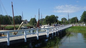 A wooden bridge over a calm water body with boats, a white railing, and greenery in the background. - Captain House South Cats 8 (Wieck auf dem Darss)