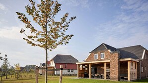 Ein modernes Haus mit Backsteinfassade, überdachter Terrasse und Rasenfläche.