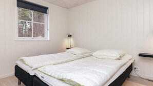 A bedroom with a bed, a window, a nightstand with a lamp, and a power outlet.