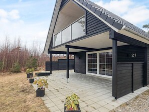 Une maison moderne avec un patio couvert, le numéro 21, et des plantes en pot.