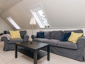 Une pièce de style loft avec un canapé gris, une table basse noire et un lampadaire. Elle est dotée de fenêtres de toit et d’une fenêtre qui laissent entrer la lumière naturelle.