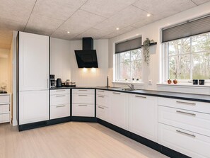 A modern kitchen with white cabinetry, a black countertop, and a window with a view of trees.
