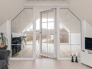 A room with a large sliding glass door leading to an outdoor deck, a television on a white stand, and a potted plant. - 6 Person Holiday Home in Laeso-by Traum (Læsø)