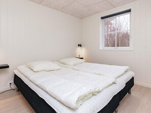 Une chambre à coucher avec un lit, une table de chevet avec une lampe, une fen être et une prise électrique au mur.