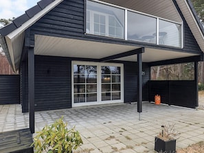 Une maison moderne de couleur noire, dotée d’un patio couvert, de grandes fenêtres et d’un numéro apparent, le « 21 ».