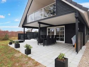 Une maison moderne dotée d’un patio couvert aménagé avec du mobilier d’extérieur et des plantes en pot.