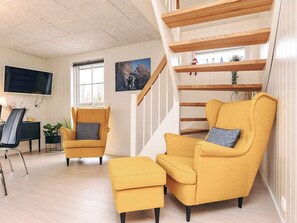 Un salon moderne avec un escalier, un téléviseur à écran plat, un coin repas et un canapé.