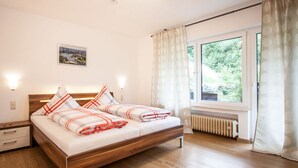 A bedroom with a wooden bed, two bedside tables, a radiator, and a window with curtains. - The Moselle Gate to Koblenz (Lehmen)