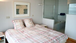 Ein Schlafzimmer mit einem Bett, einem gerahmten Bild an der Wand, einer Duschkabine aus Glas und einem kleinen Regal.