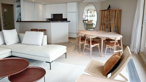 Ein modernes Wohnzimmer mit einem weißen Sofa, einem Esstisch mit Stühlen und einer kleinen Küchenzeile.