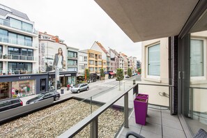 A balcony with a view of a street lined with modern buildings, including a Gibsy store and a Berry Weber store. - Apartment in Belgium Near the Sea (Koksijde)