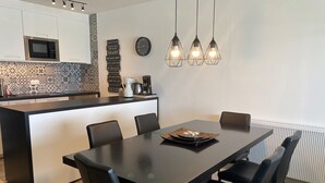 A modern kitchen with a microwave, coffee maker, and decorative tiles. There is a dining table with chairs and a clock on the wall. - Apartment in Nieuwpoort Near the Beach (Nieuwpoort)