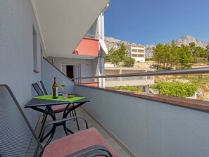 A balcony with a table set for two, a bottle of wine, and a glass. The balcony overlooks a mountainous landscape with buildings in the background. - Apartments Villa Juric - One Bedroom Apartment (Baska Voda)