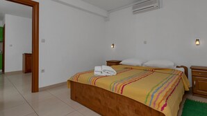 A bedroom with a wooden bed, a green rug, and a white wall with an air conditioning unit. - Apartments Villa Juric - One Bedroom Apartment (Baska Voda)