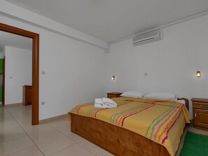 Une chambre à coucher avec un lit en bois, un tapis vert et un mur blanc sur lequel est installé un appareil de climatisation.