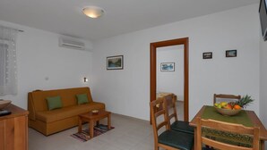 A compact living space with a sofa, a dining table with chairs, and a small side table. - Apartments Villa Juric - One Bedroom Apartment (Baska Voda)