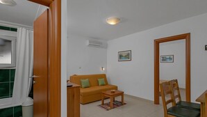 A living room with a sofa, a small table, a chair, and a dining table with chairs. - Apartments Villa Juric - One Bedroom Apartment (Baska Voda)