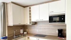 Uma cozinha compacta com armários brancos, micro-ondas, máquina de café e pia.