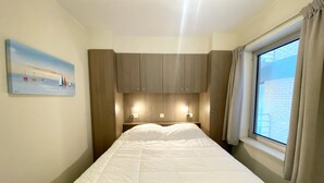 Quarto com uma cama grande, cabeceira de madeira, luminárias de cabeceira e uma janela com cortinas.