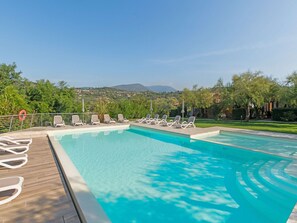 A swimming pool with lounge chairs and a view of a green landscape with trees and hills. - Belvilla by OYO Comfortable Apartment With Pool (Garda)