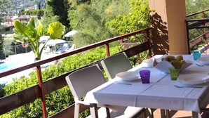 A balcony with a table set for dining, overlooking a pool and lush greenery. - Belvilla by OYO Comfortable Apartment With Pool (Garda)