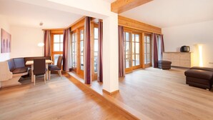 A spacious living area with a wooden floor, a sofa, a dining table with chairs, and a television on a cabinet. - Chalet in Pinzgau Near Ski Slopes (Wald im Pinzgau)
