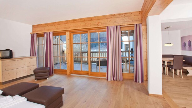 A spacious living room with a wooden ceiling, large sliding glass doors leading to a deck, a sofa, a television, and a dining area with a table and chairs. - Chalet in Pinzgau Near Ski Slopes (Wald im Pinzgau)