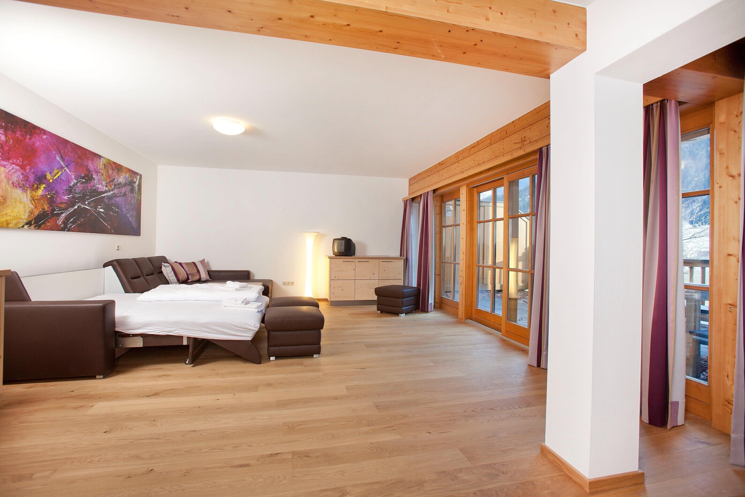 A spacious bedroom with a bed, a sofa, a desk, and a large window with curtains.