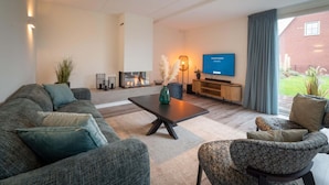 Una sala de estar moderna con sofá, sillón, mesa de centro y televisor de pantalla plana montado en la pared.