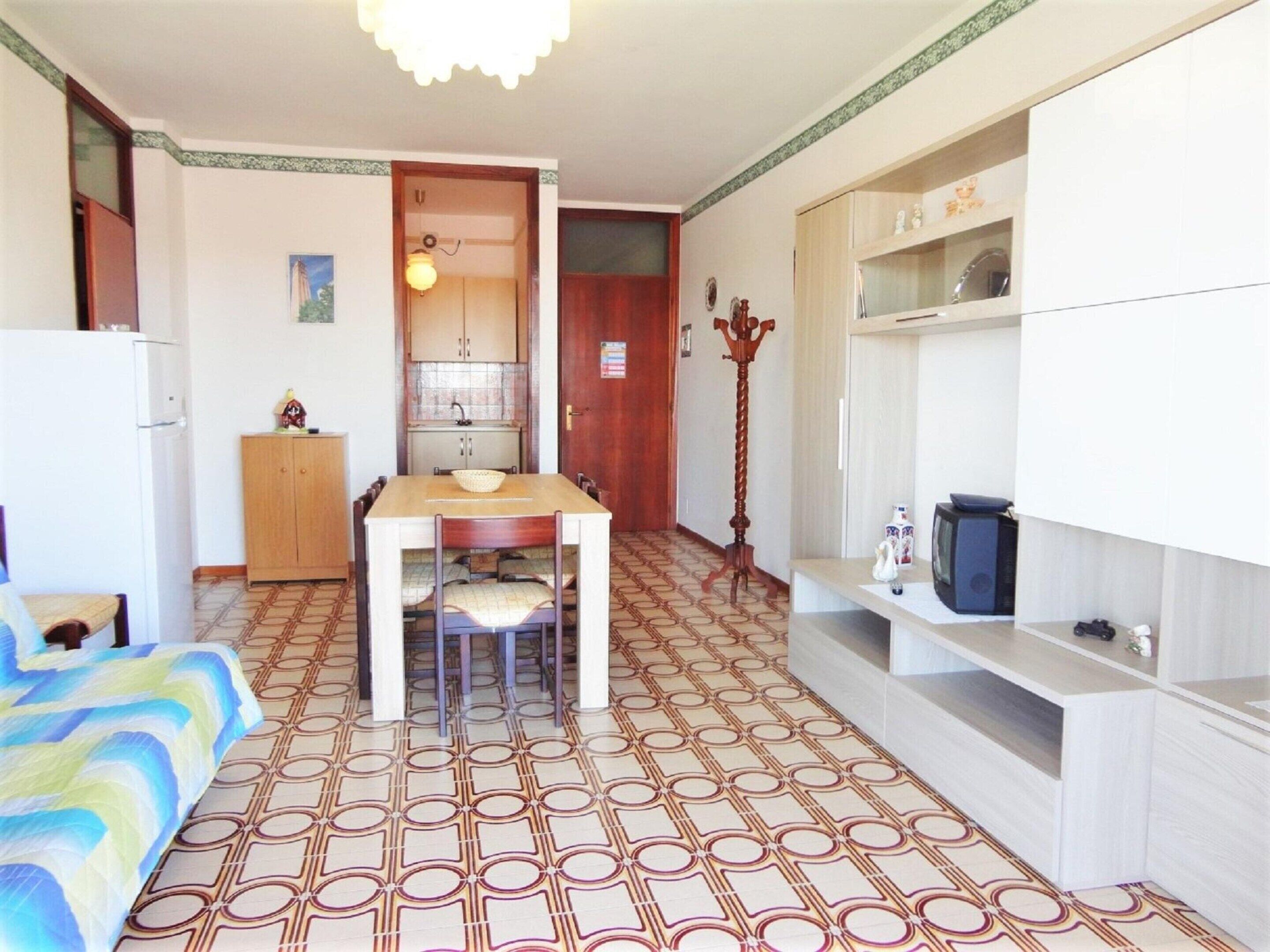 A compact room with a dining table, a sofa, a kitchenette, and a television.