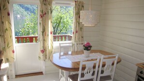 Zona pranzo con tavolo in legno e sedie bianche, un vaso con fiori e vista sul verde attraverso la finestra.