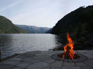 A fire pit on a stone patio by a lake with mountains in the background.