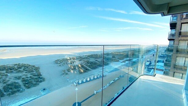 Een hoog hotel met een glazen balkon met uitzicht op een strand en een verafgelegen stadsbeeld.