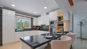 A modern kitchen with white cabinets, a granite countertop, and a central island with bar stools. - Esperanza - Javea, Costa Blanca (Javea)
