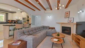 A modern living room with a sectional sofa, a fireplace, a TV, and a kitchen in the background. - Esperanza - Javea, Costa Blanca (Javea)