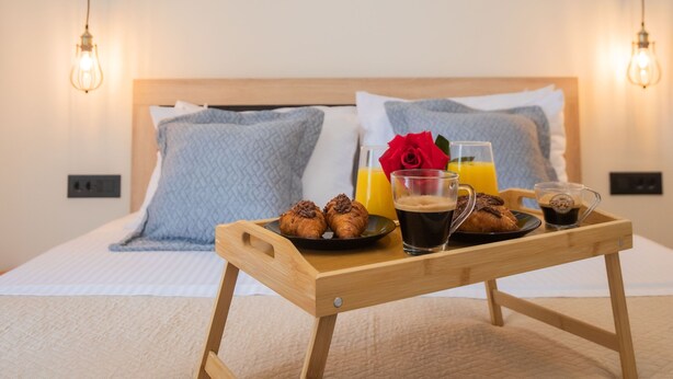 A neatly made bed with a wooden bedside table holding croissants, coffee, and orange juice. - Calliope's Rhodes City Comfort (Rhodes)