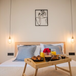 A neatly made bed with a wooden bedside table holding croissants, coffee, and orange juice. - Calliope's Rhodes City Comfort (Rhodes)