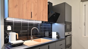 A modern kitchen with a black countertop, stainless steel appliances, and wooden cabinets. - Calliope's Rhodes City Comfort (Rhodes)