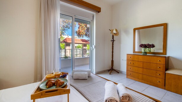 A hotel room with a bed, a wooden dresser, a mirror, a tray with croissants and juice, and a view of a balcony with a railing and trees. - Mike s House in Kremasti Near the Beach Rhodes (Rhodes)