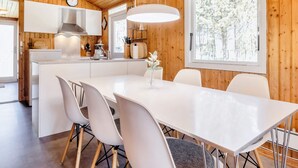 A modern kitchen with wooden walls, a central island, white cabinetry, and a dining area with a white table and chairs. - 6 Person Holiday Home in Strandby (Strandby)